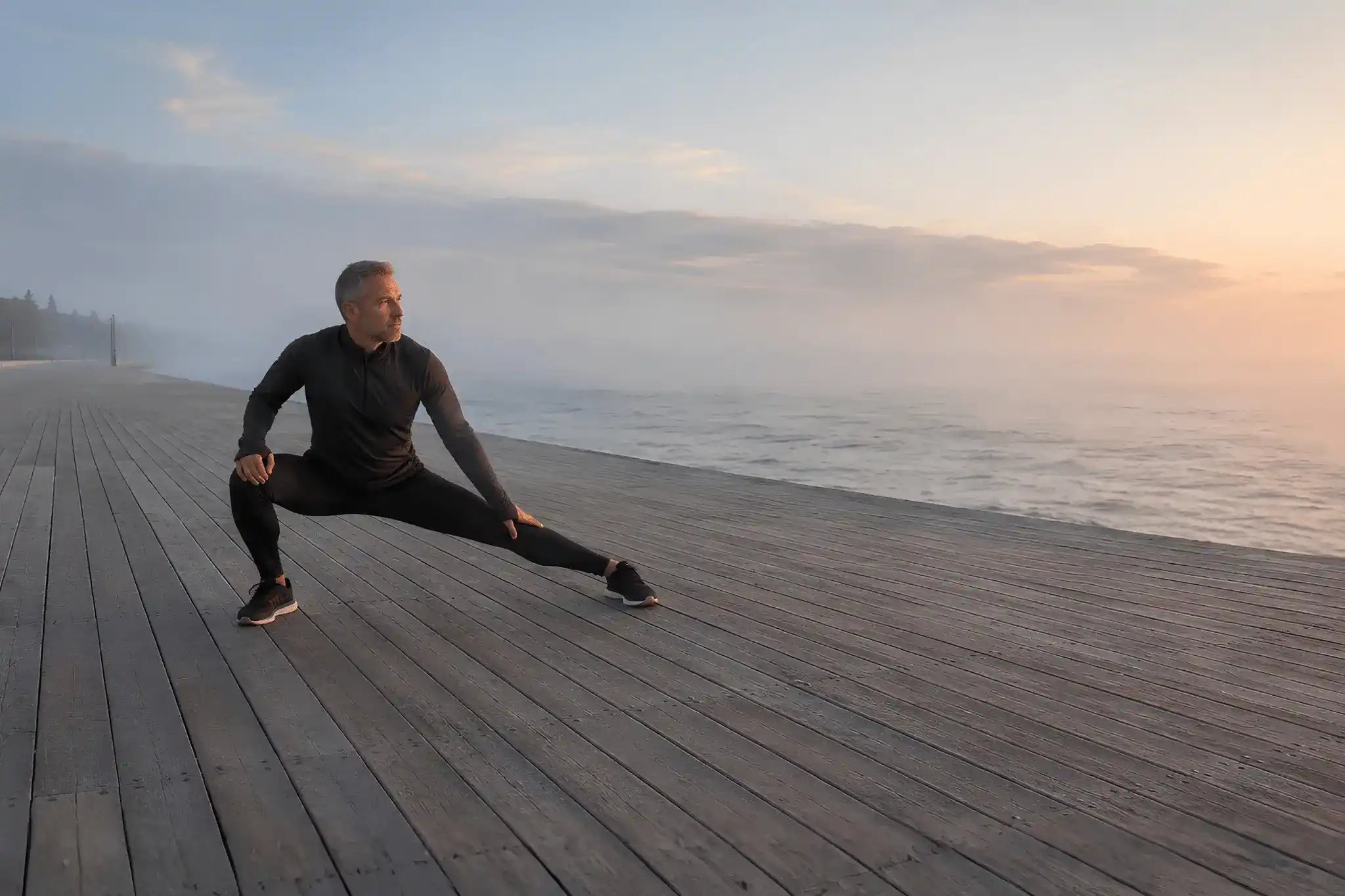 Hombre mayor de 40 años estirando hombro y torso en un jardín al atardecer.